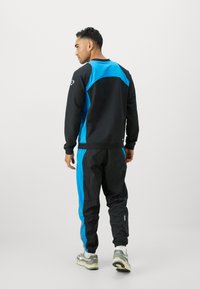 Sort og blå sportstrækningsdragt med kontrasterende paneler, der består af en crew neck sweatshirt og tapered bukser med elastiske manchetter.