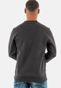 Sweat-shirt gris foncé avec un col rond et des poignets côtelés. Présente une texture lisse et semble être une coupe décontractée avec des détails de conception minimaux.