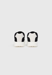 Adidas negru și alb cu un superior din țesătură netedă, panouri contrastante, guler căptușit și talpă de cauciuc albă. Design curat, modern.