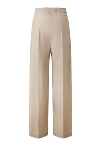 Beige wijde broek met een elastische tailleband, voorzien van plooien en een gladde textuur. De zoom is iets taps toelopend, wat zorgt voor een nette afwerking.