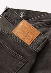 Grå denimbukser med et lærmerke som har "Levi Strauss & Co." sydd på. Sydde lommer og detaljerte sømmer langs sømmene.