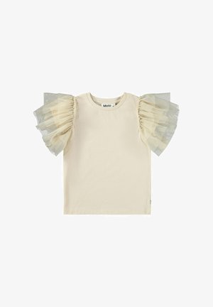Camiseta de color crema con mangas cortas, que presenta detalles de volantes transparentes en tul beige claro y gris en ambos hombros. Etiqueta de la marca visible.