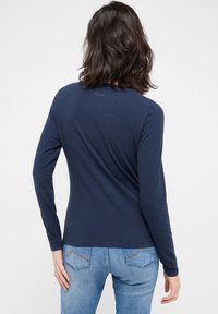 Langärmliges, marineblaues Hemd aus weichem Stoff. Hat einen runden Halsausschnitt und eine lockere Passform. Kombiniert mit hellblauen Jeans aus Denim mit Teilungsnähten.