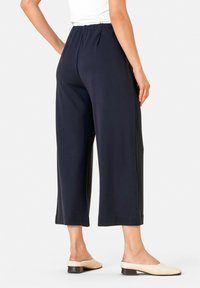 Navy wijde broek gemaakt van zachte stof, met een ontspannen taille en een cropped lengte, gecombineerd met crèmekleurige muiltjes met een lage hak.