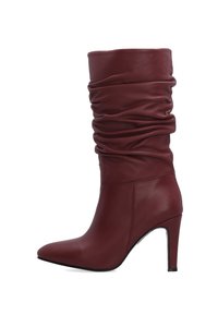 Kozačky z burgundské kůže do poloviny lýtek se zúženým kotníkem, špičatou špičkou a vysokým stiletto podpatkem, zobrazené z boku na bílém pozadí.