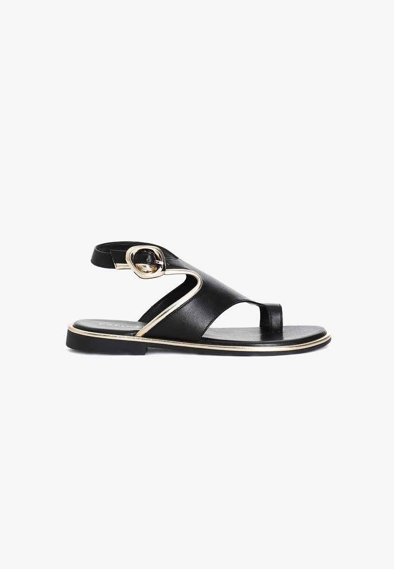 Musta nahkainen sandaali, jossa on tasapohja, ainutlaatuinen leikkauksellinen muotoilu, kultaiset korostukset ja koristeellinen solki hihnassa.