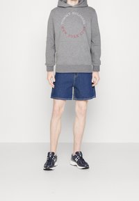 Grauer Kapuzenpulli mit "TOMMY HILFIGER NEW YORK CITY" Logo, kombiniert mit blauen Denim-Shorts und navyblauen Turnschuhen mit weißen Akzenten.