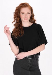 Černý top s krátkým rukávem, kulatým výstřihem a nabíranými rukávy, kombinovaný s tmavě modrou riflovou sukní s vysokým pasem, která má hladkou texturu.