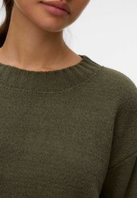 Suéter verde oliva con un tejido texturizado, presentando un escote redondo y borde acanalado. Tejido suave con detalles de costura visibles.