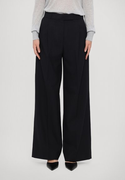 Zwarte pinstripe wijde pijpen broek met een hoge taille, voorzien van scherpe frontplooien en een gladde textuur, gecombineerd met spitse zwarte schoenen.