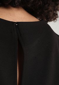 Svart tyg med slät textur, med en liten öppning bak och en diskret dragkedjestängning.