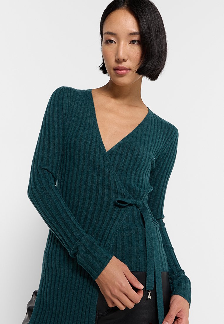 Cardigan avvolgente a coste teal con maniche lunghe e una cintura in vita. Realizzato in materiale morbido, presenta un profondo scollo a V.