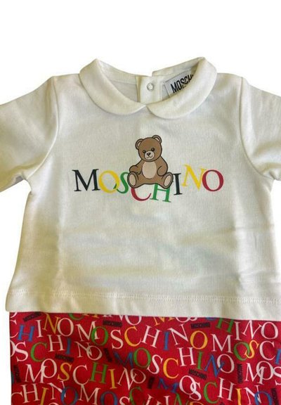 Biała koszulka z krótkim rękawem z grafiką niedźwiedzia i napisem "MOSCHINO" w kolorowych literach, zestawiona z czerwonymi szortami z wielokolorowym wzorem logo.