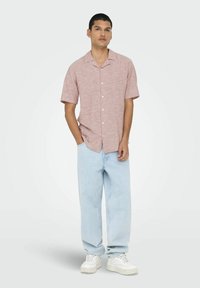 Camisa de manga corta de color rojo y blanco con un cuello tipo solapa, combinada con vaqueros ajustados de color azul claro y zapatillas blancas.