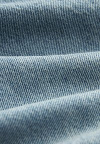 Ljust blå denimtyg med twillbinding, som har en mjuk struktur och synliga sömmönster längs veckarna.