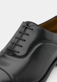 Zapato oxford de cuero negro con un acabado suave, diseño de cordones de siete ojales y una puntera redondeada con una ligera curva.
