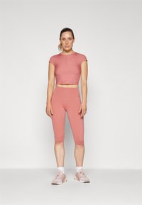 Rózsaszín sportos crop top és hozzá illő capri leggings, rugalmas anyagból készült, visszafogott logóval és testhez simuló fazonnal.