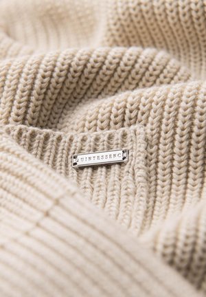 Tessuto in maglia beige con un motivo a coste testurizzato, dotato di un'etichetta argento con la scritta "QUINTESSENCE" attaccata. Il materiale appare morbido e accogliente.