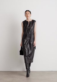 Schwarzes ärmelloses Kleid aus glänzendem Kunstleder, mit elastischem Bund, gerader Silhouette und einem dezenten Ausschnitt.