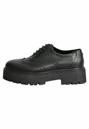 Chaussures à lacets en cuir noir présentant un design brogue avec une semelle épaisse et robuste ainsi qu'une finition texturée. Découpes décoratives le long de la tige.