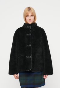 Chaqueta de piel sintética negra con un cuello alto, cinco botones y bolsillos laterales. Diseñada con una textura suave y una silueta relajada y de gran tamaño.