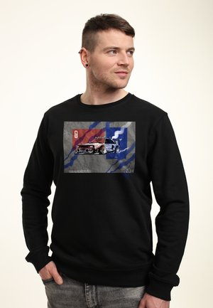 Zwarte sweatshirt met een grafische afbeelding van een gedetailleerde raceauto tegen een grijs, rood en blauw achtergrond. Zacht materiaal met geribde manchetten.
