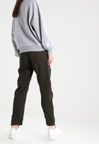Szary, oversize sweatshirt z obniżonymi ramionami w połączeniu z oliwkowymi joggerami z elastycznymi mankietami i kieszeniami, noszony z białymi sneakersami.