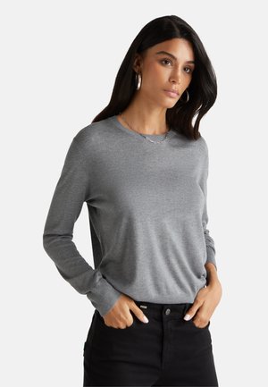 Grijze lange mouw sweater met een ribbelboord bij de hals en mouwen, gedragen over zwarte broek, met een gladde textuur en een relaxte pasvorm.