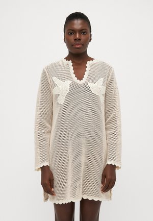 Krämfärgad mesh-overall med en scalloperad halsringning och ärmar. Har två vita fågelmotiveringar på framsidan. Lätt och texturerad.