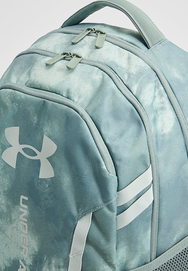 Zaino azzurro chiaro realizzato in tessuto testurizzato con doppie cerniere, logo Under Armour e accenti a righe bianche. Design sagomato con schiena imbottita.