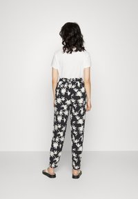 Pantalones negros con patrones de hojas blancas, cinturilla elástica y piernas ajustadas. Combinados con una camiseta blanca y sandalias negras.