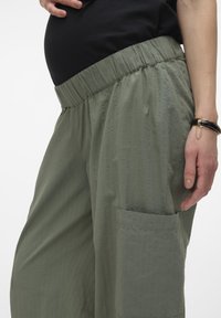 Zwangertrousers in textuurrijke olijfgroene stof, met een brede, elastische tailleband en een zijzak. Gladde afwerking met verticale strepen.