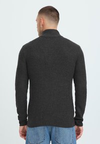 Mørkegrå strikket sweater med højt krave, ribbede manchetter og struktureret mønster. Designet med en tætsiddende silhuet.