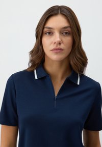 Marineblauwe poloshirt met een kraag en een korte rits, voorzien van witte accenten op de kraag. Zachte, lichte stof.