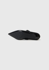 Zapato de tacón negro con puntera afilada, suela texturizada y acabado suave. Cuenta con una correa ajustable para un mejor ajuste y estabilidad.