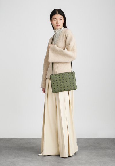 Zelená kabelka so vzorom vyrobená z textúrovaného materiálu. Obdĺžnikový tvar s dlhým popruhom, držaná na neutrálnej pozadí.