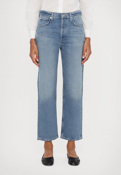 Jeans anchos de mezclilla de color azul claro con cintura alta, diseño de cinco bolsillos y dobladillo ligeramente deshilachado, combinados con bailarinas negras.