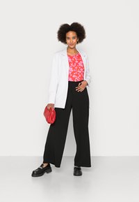 Blazer branco sobre uma blusa floral vermelha, combinado com calças largas pretas e sapatos chunky pretos. Acessorizado com uma bolsa pequena vermelha.
