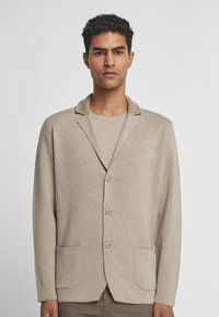 Beiger Blazer aus weichem Stoff, mit Reverskragen, drei Knöpfen und zwei vorderen Taschen mit glatter Textur.