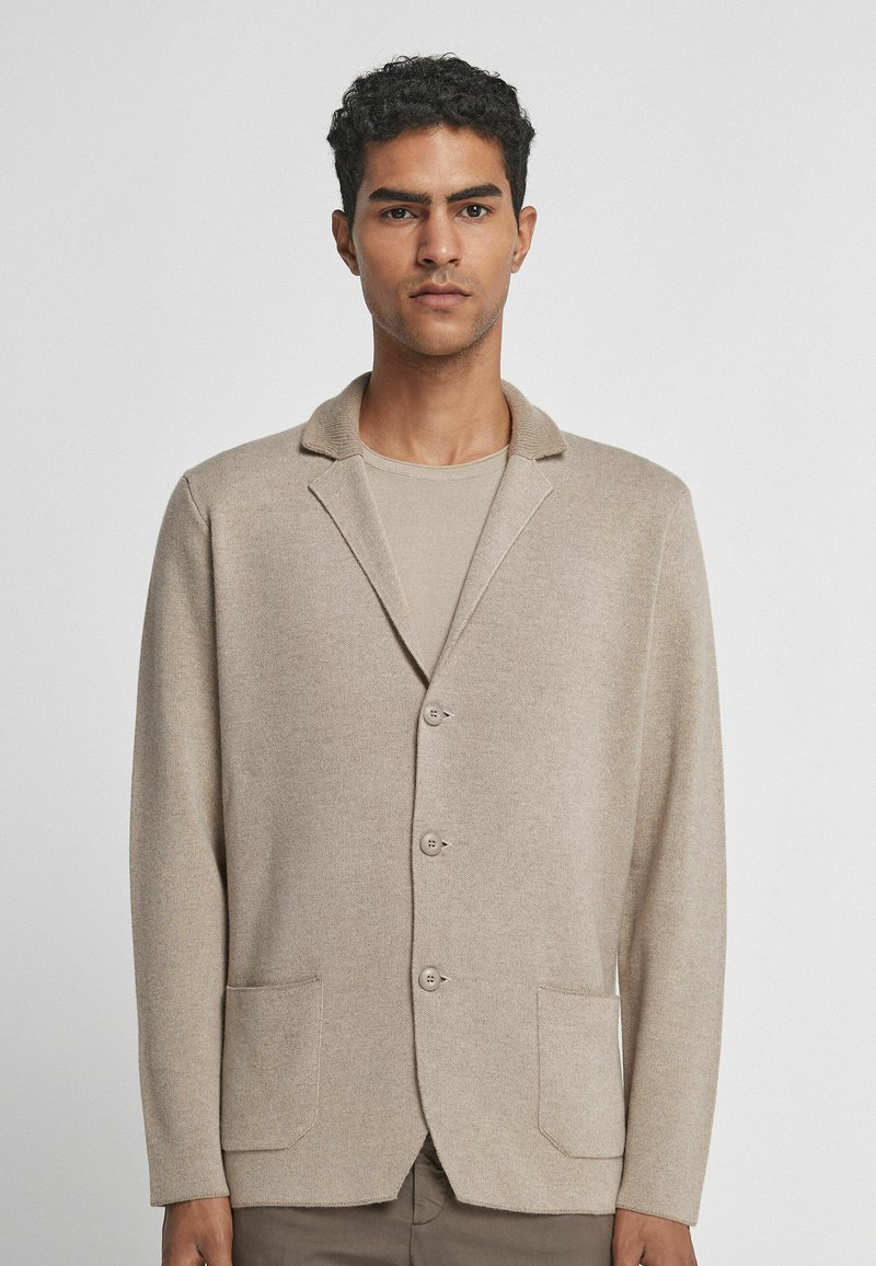 Beiger Blazer aus weichem Stoff, mit Reverskragen, drei Knöpfen und zwei vorderen Taschen mit glatter Textur.