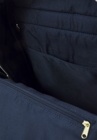 Mörkblå tygväska med insida som har blixtlåsförslutning. Har en slät yta och en extra ficka inuti. Guldiga blixtlåshandtag synliga.