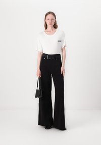 Witte T-shirt met korte mouwen en zwart "HUGO" logo, gecombineerd met hoogwaisted zwarte flared broeken en een kleine zwarte handtas.