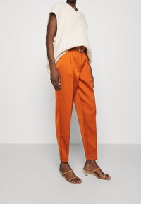 Crème, geribbeld gebreid oversized sweater met V-hals; gecombineerd met oranje op maat gemaakte broek met plooien; naakt kleurige strappy hakken.