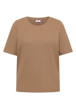 Femme aux cheveux courts bruns portant une casquette de baseball rose et un haut beige côtelé ajusté à manches courtes, souriant légèrement de côté.