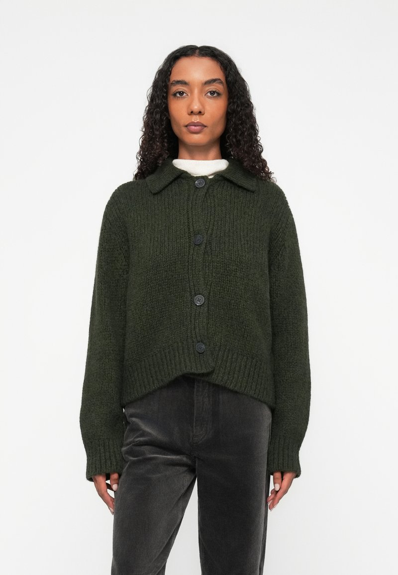 Cardigan tricotat de culoare verde închis, cu guler, cinci nasturi negri și o croială lejeră. Materialul texturat și designul scurt adaugă interes vizual.