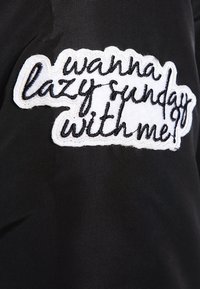 Czarna tkanina posiada biały wyszywany naszywkę z napisem "chcesz leniwe niedziele ze mną?" w swobodnej, odręcznej czcionce.