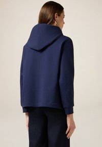 Granatowa bluza z kapturem o krojonej konstrukcji, miękka w dotyku, z długimi rękawami, charakteryzująca się luźnym krojem i detalem w postaci szycia na krawędzi.