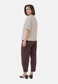 Striped cream and brown t-shirt with short sleeves paired with burgundy trousers. The model wears dark heeled shoes, showcasing a casual look.