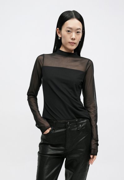 Top preto de manga comprida com parte superior em malha transparente, secção intermédia preta sólida e design ajustado. Usado com calças de couro pretas de cintura alta.