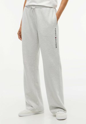 Lichtgrijze wijd uitlopende joggingbroek met trekkoord in de taille en Tommy Hilfiger-logo op de linker dij, gedragen met witte sneakers.